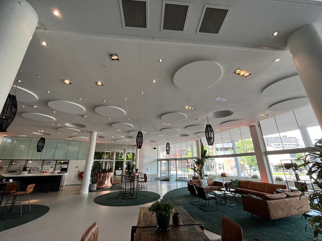 Akoestische verbetering van een evenementenlocatie met stijlvolle plafondeilanden. De eilanden verminderen galm en echo, waardoor spraakverstaanbaarheid helder is tijdens bijeenkomsten en evenementen.